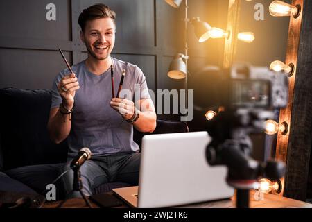 Der junge lächelnde Blogger zeigt Make-up-Pinsel Stockfoto