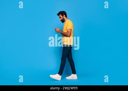 indischer Mann mittleren Alters in gelbem Gehen und SMS am Telefon Stockfoto