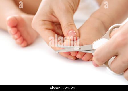 Mutter hält den Fuß des kleinen Kindes und schneidet die Zehennägel. Stockfoto