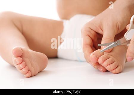 Mutter hält den Fuß des kleinen Kindes und schneidet die Zehennägel. Stockfoto