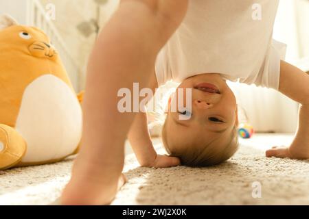Kleiner Junge im Body, der kopfüber auf einem Schlafzimmerboden steht. Stockfoto
