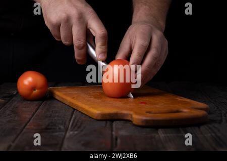 Gemüse schneiden. Männliche Hände schneiden Tomaten auf einem Schneidebrett Stockfoto