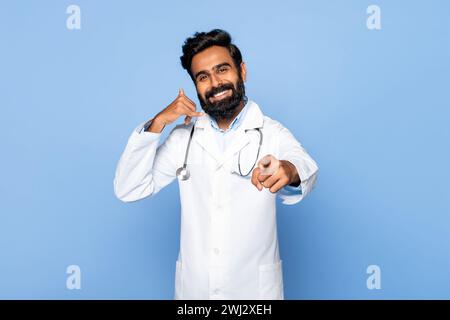 Fröhlicher indischer Arzt mittleren Alters, der mich vor blauem Hintergrund anruft Stockfoto
