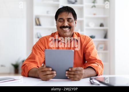 Lächelnder reifer indischer Unternehmer, der einen digitalen Tablet-pc verwendet Stockfoto