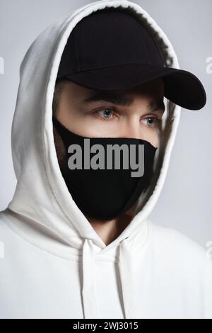 Mann mit weißem Hoodie, schwarzer Baseballmütze und Stoffmaske Stockfoto