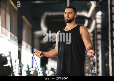 Konzentrierter tätowierter männlicher Athlet mit Sprungseil in den Händen, der im Fitnessstudio steht Stockfoto