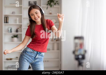 Junge asiatische Frau mit Kopfhörern, die zu Hause tanzen und Videos aufzeichnen Stockfoto