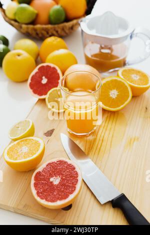 Geschnittene Zitrusfrüchte und ein Glas frischer Orangensaft auf dem Schneidebrett Stockfoto
