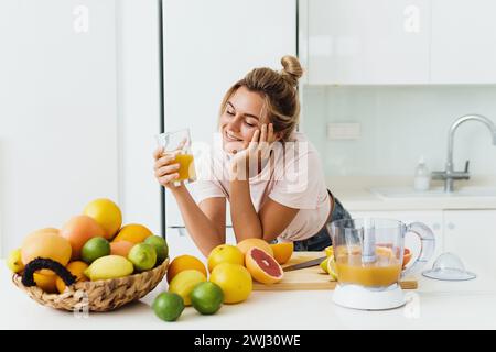 Frau, die frisch gepressten, selbstgemachten Orangensaft in der weißen Küche trinkt Stockfoto