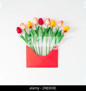 Frühlingskomposition mit bunten Tulpenblüten aus rotem Umschlag auf weißem Hintergrund. Minimales Konzept. Kreative Frühlingsblumen-Idee. Stockfoto