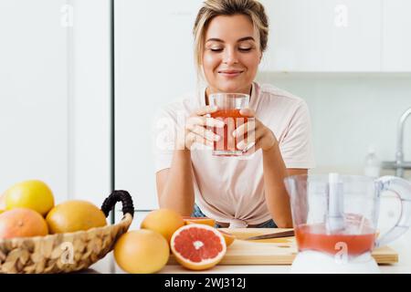 Frau, die frisch gepressten hausgemachten Grapefruitsaft in der weißen Küche trinkt Stockfoto