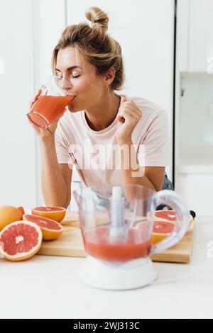 Frau, die frisch gepressten hausgemachten Grapefruitsaft in der weißen Küche trinkt Stockfoto