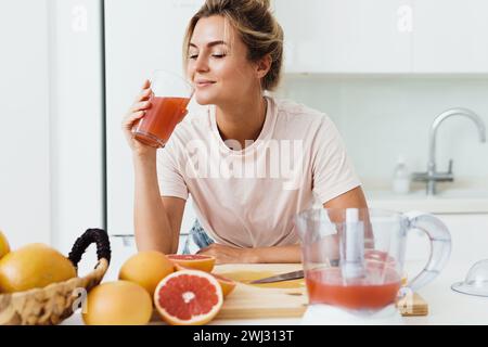 Frau, die frisch gepressten hausgemachten Grapefruitsaft in der weißen Küche trinkt Stockfoto