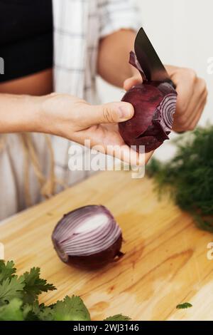 Weibliche Hände mit einem Messer, das während des Kochens rote Zwiebeln schält Stockfoto