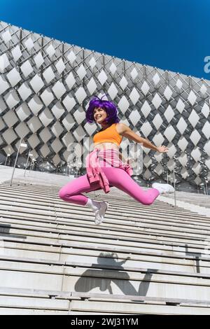 Sorglose Frau in farbenfroher Sportswear, die während des Sommertages auf die Straße springt Stockfoto