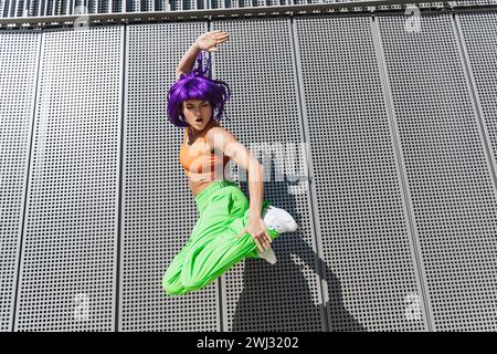 Sorglose Frau in farbenfroher Sportswear, die während des Sommertages auf die Straße springt Stockfoto