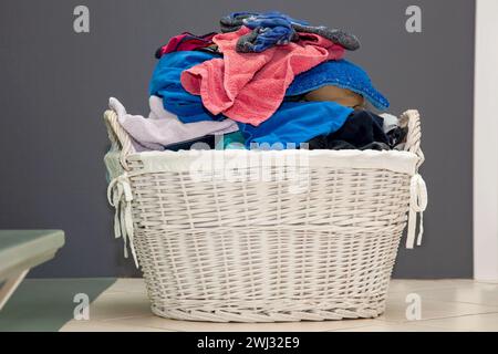 Holzkorb mit dreckiger Wäsche auf dem Boden. Kleidung im Rattankorb. Bunte, schmutzige Wäsche gelesen Stockfoto