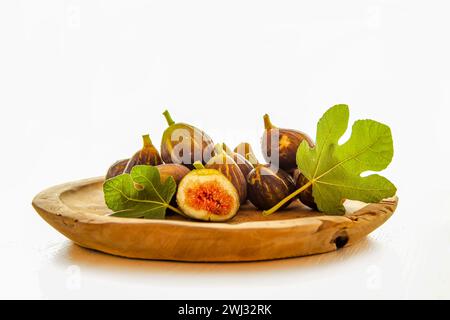 Frische rohe Feigenfrüchte und geschnittene Portion und Feigenblatt auf einem Tisch, auf einem Holzteller isoliert Stockfoto