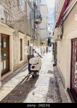 Budva, Montenegro – 17. august 2023: Mann in einem Helm fährt einen Roller in seinen Händen entlang einer engen Steinstraße einer antiken Stadt Stockfoto