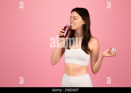 Eine gesundheitsbewusste Frau in weißer Sportswear genießt einen frischen Rote-Bete-Saft, während sie einen Flaschendeckel hält Stockfoto