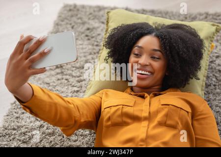 Eine fröhliche Afroamerikanerin mit einem lebhaften Lächeln liegt auf einem Kissen Stockfoto