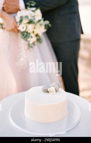 Der Bräutigam umarmt die Braut in der Nähe der Hochzeitstorte auf einem Stand auf dem Tisch. Abgeschnitten. Gesichtslos Stockfoto