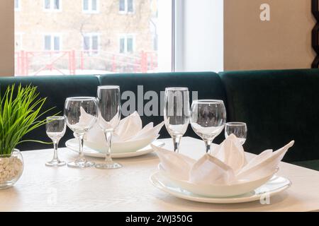 Gläser, Teller, Servietten werden zum Abendessen in einem Restaurant mit gemütlicher Einrichtung serviert. Gläser und Teller auf einem Tisch im Restaurant serviert zum Abendessen. Stockfoto