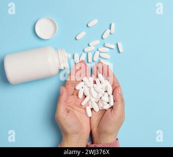 Die Hand einer Frau, die eine Plastikflasche und weiße ovale Pillen auf blauem Hintergrund hält, von oben. Stockfoto