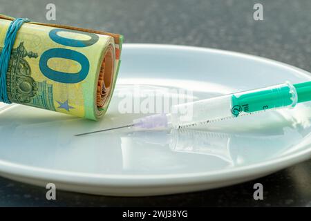 100- und 50-Euro-Scheine, die mit einem Gummiband verbunden sind. Spritze Und Eurogeld Auf Weißer Platte. Arzneimittelsucht Stockfoto