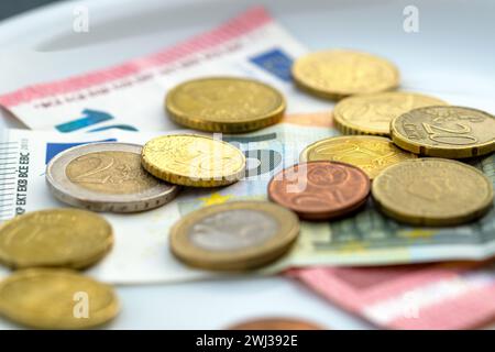 Nahaufnahme von Münzen und Währungsschein auf Platte. Hochwinkelansicht. Euro-Geld auf weißer Platte. Platte mit Stockfoto