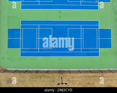 Luftbild von ungewöhnlich bemalten blauen Tennisplätzen im Freien mit gelben Pickleball-Linien und grünem außerhalb der Grenzen. Stockfoto