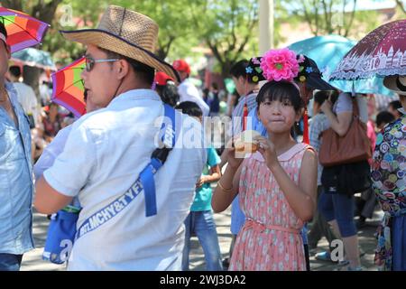 Füttern Von China. Ein Teenager auf einer Straße in Peking, ein chinesisches Mädchen mit Dekorationsblume auf dem Kopf isst neben Dad ein Brötchen mit Sahne. Stockfoto