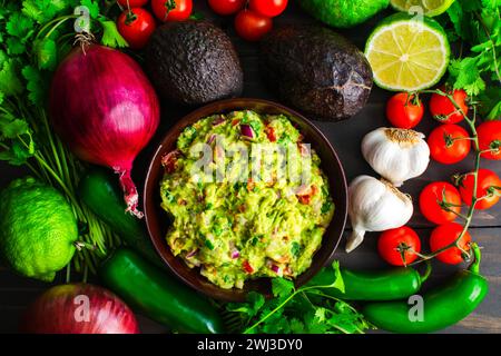 Schüssel Guacamole umgeben von frischen Zutaten: Guacamole mit Hass Avocados, Jalapeno Paprika, Kirschtomaten und anderen Zutaten Stockfoto