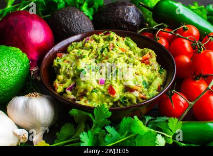 Schüssel Guacamole umgeben von frischen Zutaten: Guacamole mit Hass Avocados, Jalapeno Paprika, Kirschtomaten und anderen Zutaten Stockfoto
