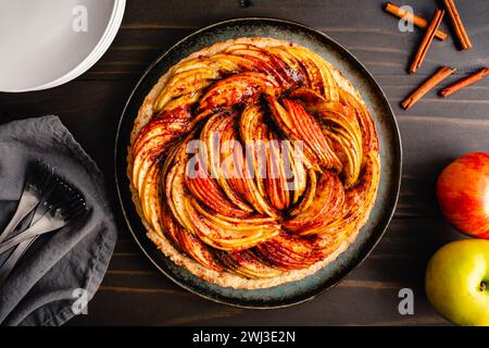 Gebackene vegane Apfeltorte mit Tellern und Gabeln auf einem Holztisch: Eine Tarte aus Zimt, in Scheiben geschnittenen Ambrosia, Golden Delicious und Granny Smith Äpfeln Stockfoto