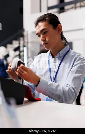 Asiatischer Manager faltet modische Krawatten in einer modernen Boutique, arbeitet im Geschäft Visual. Fröhlicher, stilvoller Angestellter, der neue Modekollektion arrangiert und den Preis für Kleidung im Einkaufszentrum überprüft Stockfoto