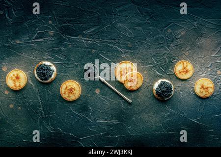 Blinis mit schwarzem Kaviar und Frischkäse über dem Kopf flach auf Schwarz Stockfoto