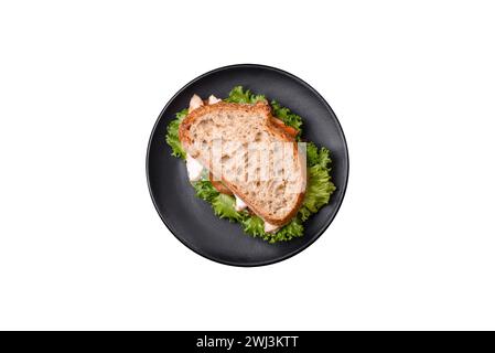 Frisches, leckeres Sandwich mit Huhn, Tomaten und Salat auf einem schwarzen Teller Stockfoto