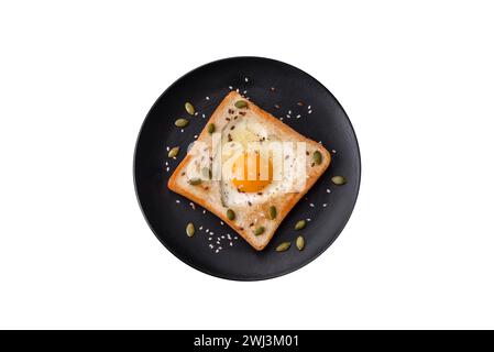 Herzförmiges Spiegelei in Brottoast mit Sesamsamen, Leinsamen und Kürbiskernen auf einer schwarzen Platte Stockfoto