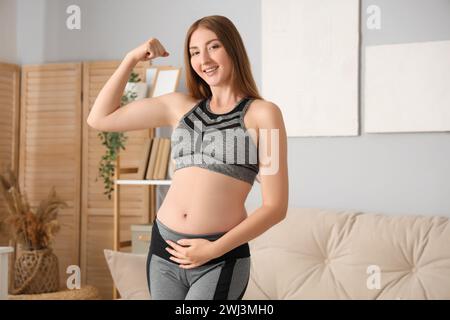 Sportliche junge schwangere Frau, die zu Hause Muskeln zeigt Stockfoto