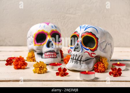 Bemalte menschliche Schädel mit brennenden Kerzen und wunderschönen Blumen für Mexikos Tag der Toten auf weißem Holztisch Stockfoto