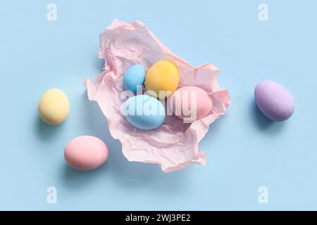 Zerknittertes Papier mit bemalten Ostereiern auf blauem Hintergrund Stockfoto