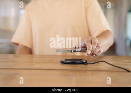 Laden des Mobiltelefonakkus mit drahtlosem Ladegerät im Tisch. Smartphone wird auf einem Ladepad aufgeladen. Mobiltelefon ne Stockfoto