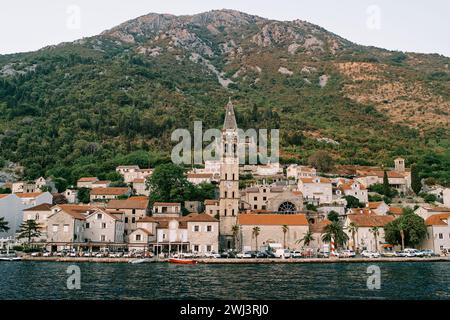 Blick vom Meer auf den Glockenturm der Kirche St. Nikolaus zwischen alten Häusern am Fuße der Berge. Perast, Mo Stockfoto