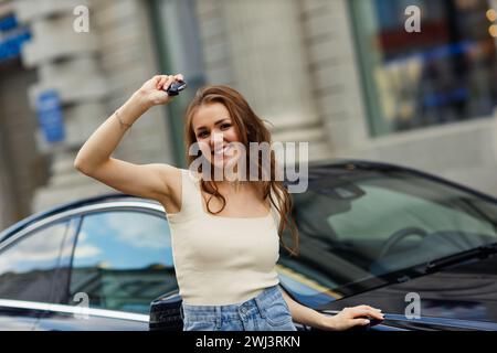 Eine glückliche Fahrerin hält die Schlüssel und lächelt. Süße junge glückliche brünette Frau, die Auto fährt. Stockfoto