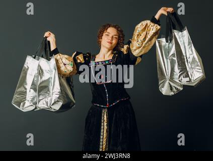 Junge Erwachsene Frau in einem mittelalterlichen Kleid, die Einkaufstaschen in den Händen hält Stockfoto