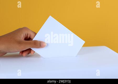 Stimmende Frau in der Nähe der Wahlurne auf gelbem Hintergrund, Memasukkan Surat Suara Stockfoto