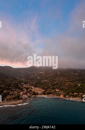 Drohnenblick auf Seccheto Beach und Dorf auf Elba Island kurz nach Sonnenuntergang mit einem nebligen lila Himmel Stockfoto