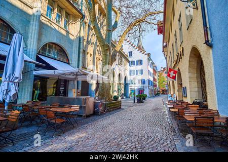 ZÜRICH, SCHWEIZ - 3. APRIL 2022: Schattig in der Gassen Straße mit Terrassentischen von Restaurants, am 3. April in Zürich, Schweiz Stockfoto