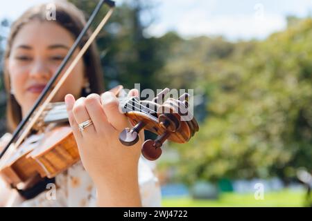 Nahaufnahme des Weitwinkelbildes einer unscharfen lateinischen jungen Buskerin, die im Freien Geige spielt, Fokus auf den Geigenhals und die Muschel mit klarem Himmel im Hintergrund Stockfoto